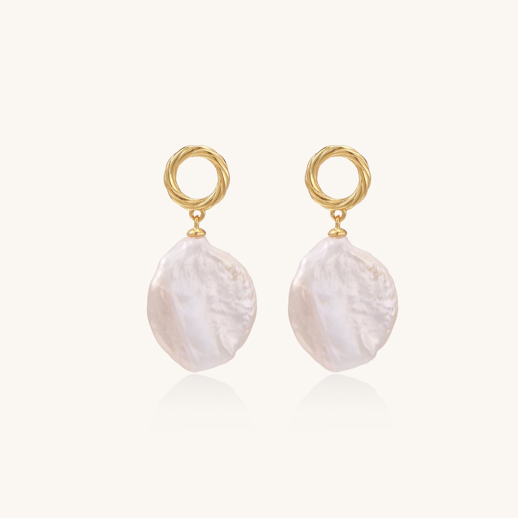 Gold-plated twisted stud earrings with large blush baroque pearls hanging elegantly on white background.