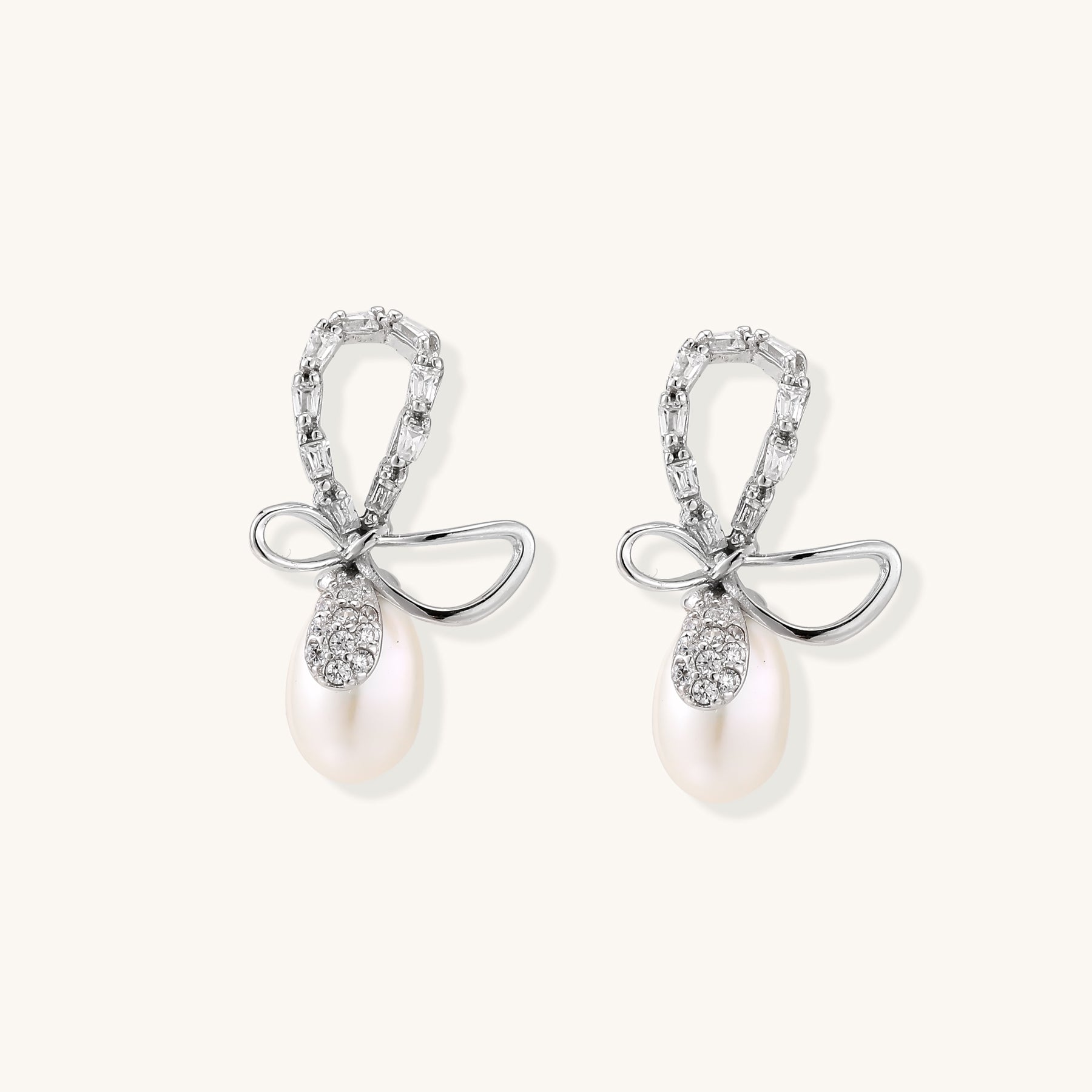 Sterling silver stud earrings with baguette crystal bow design and freshwater pearl drops on white background