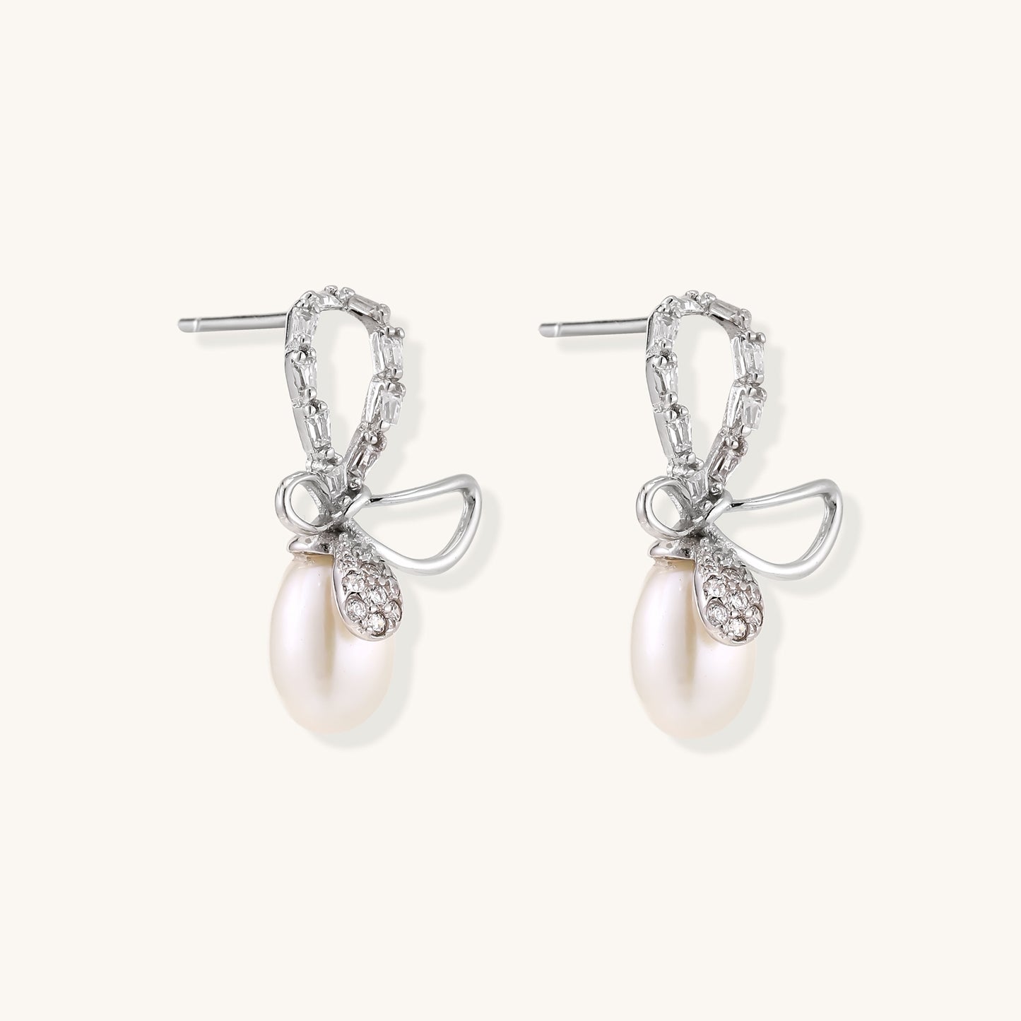 Sterling silver stud earrings with baguette crystal bow design and freshwater pearl drops on white background
