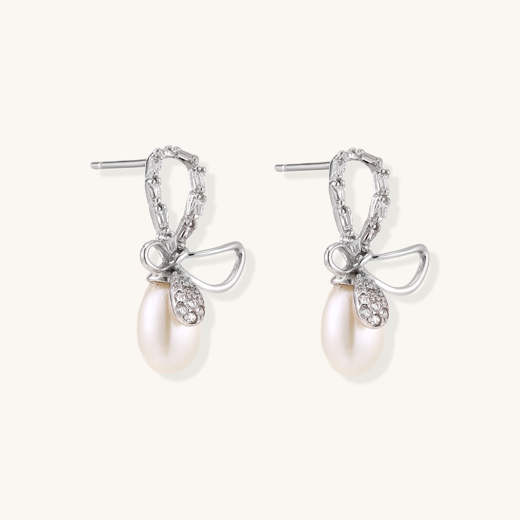 Sterling silver stud earrings with baguette crystal bow design and freshwater pearl drops on white background