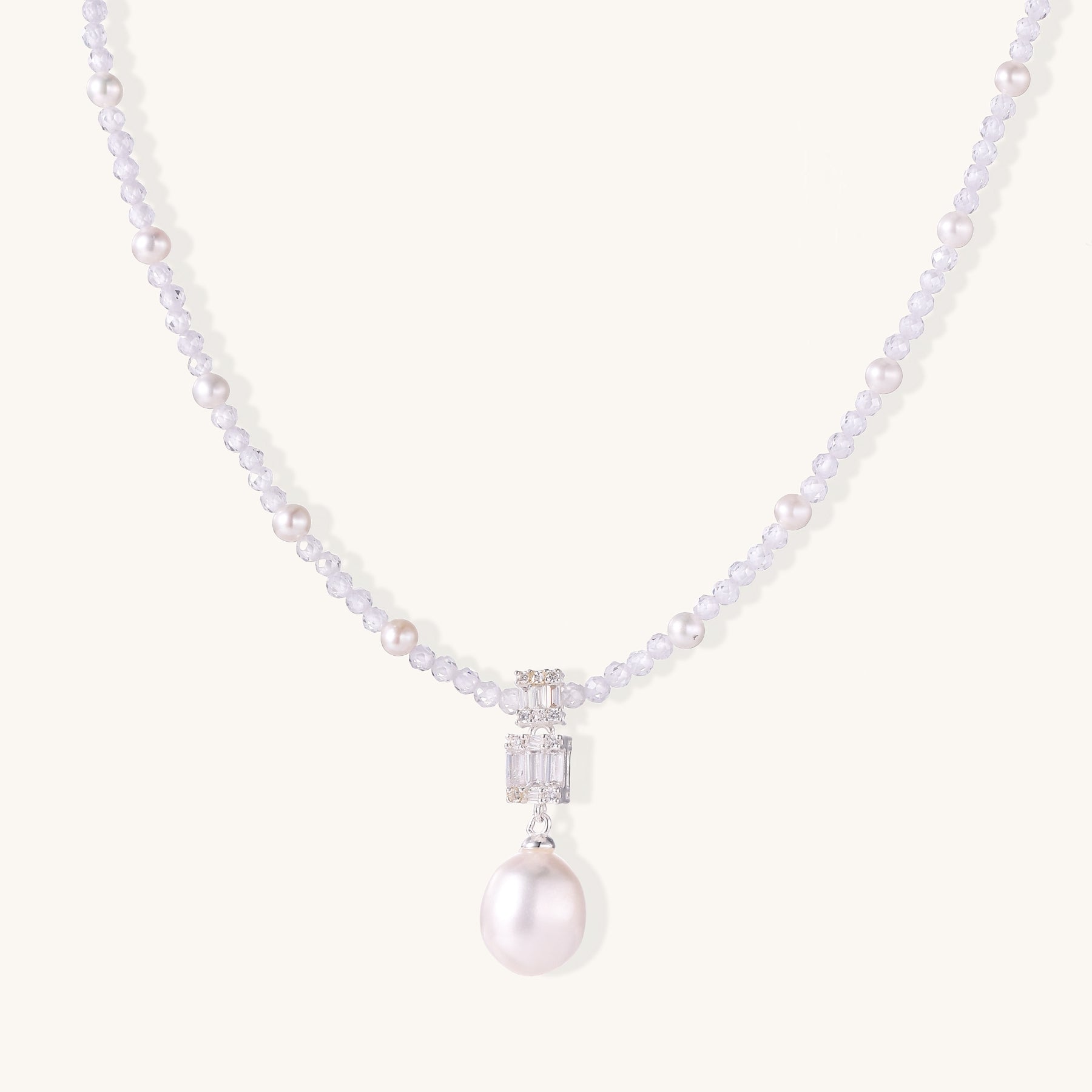 Delicate beaded necklace with lavender crystals, white pearls, and crystal pendant with pearl drop on white background.