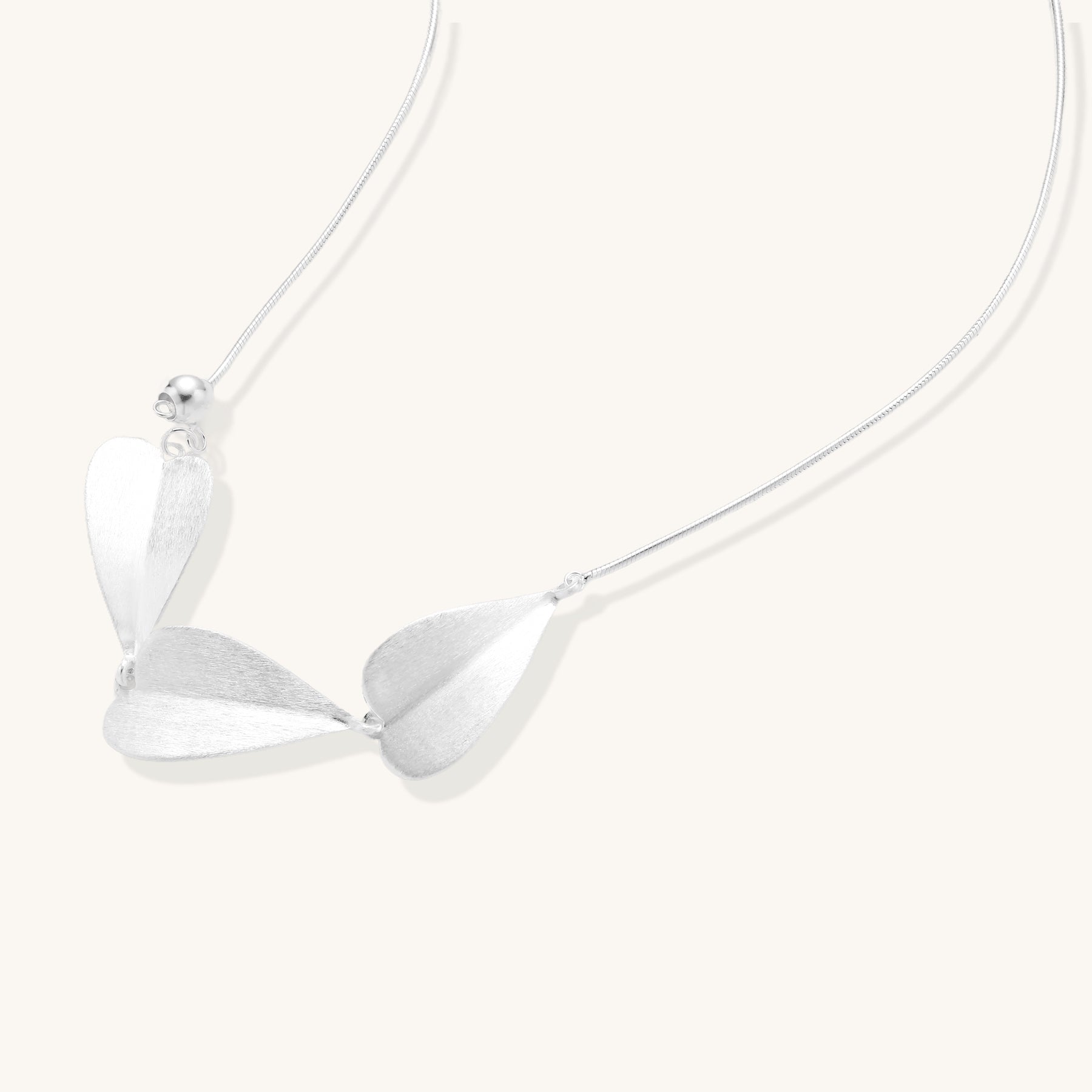 Delicate sterling silver necklace with brushed leaf pendants distributed along a fine chain on white background.