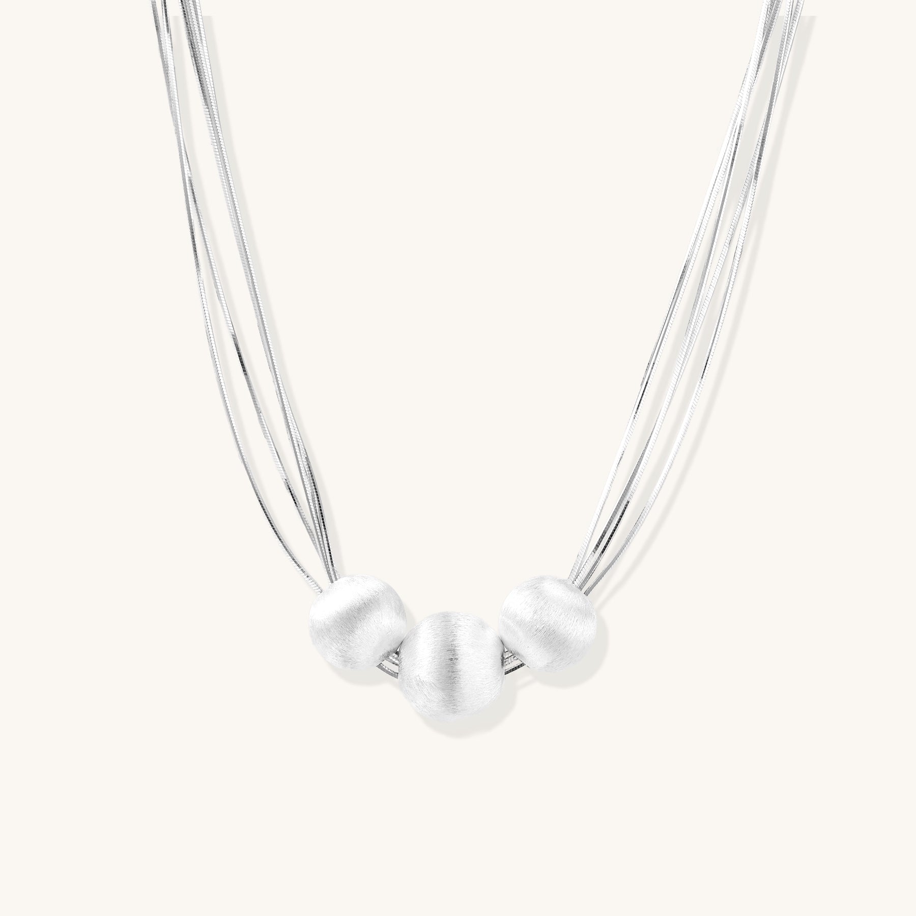 Multi-strand sterling silver necklace with three polished round beads clustered at center on white background.