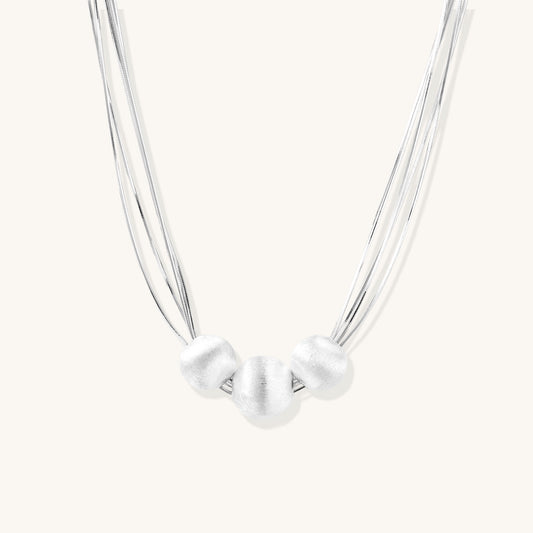 Multi-strand sterling silver necklace with three polished round beads clustered at center on white background.