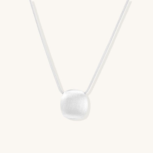 Minimalist sterling silver necklace with brushed square pendant on adjustable chain against white background.
