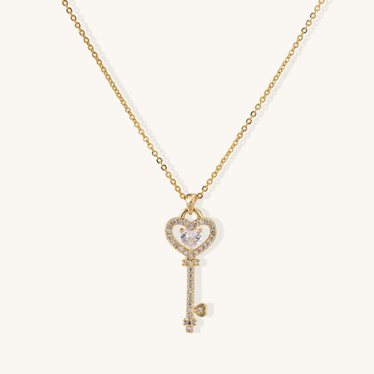Gold-plated key pendant necklace with heart top and crystal embellishments on adjustable chain against cream background