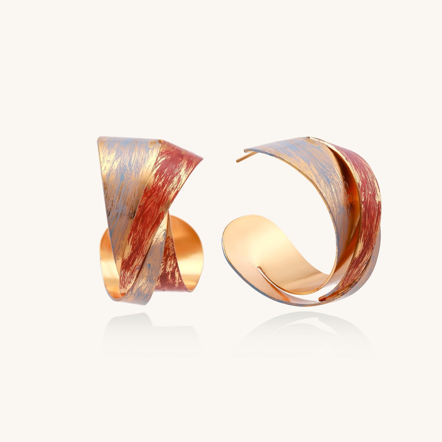 Twisted gold-plated brass earrings with multicolored enamel brushstroke patterns in burgundy and blue on white background.