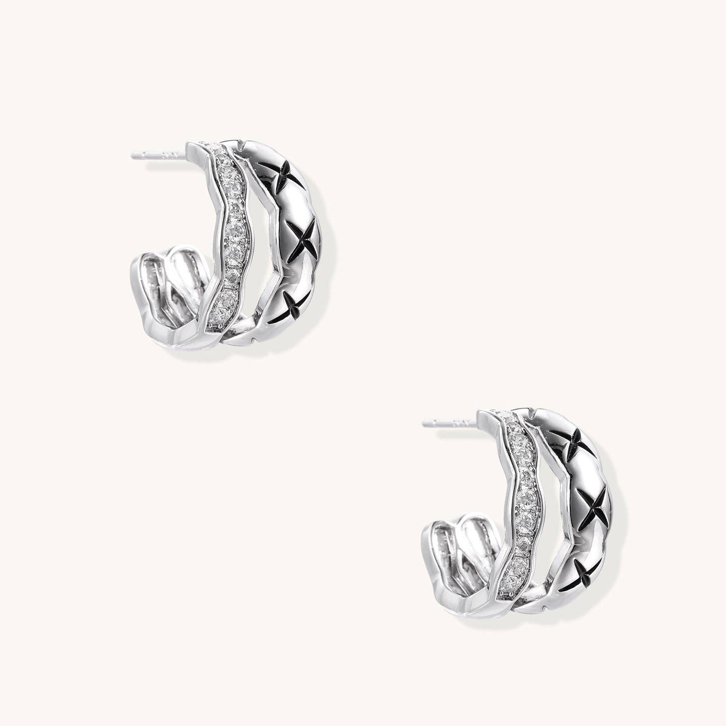 Close-up of gold-plated huggie earrings featuring X-pattern band and wavy zirconia-set band on white background.