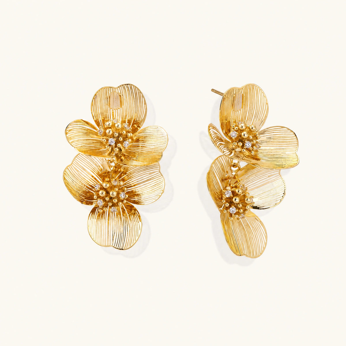 Pair of gold-plated double flower earrings with textured petals and crystal centers on cream background.