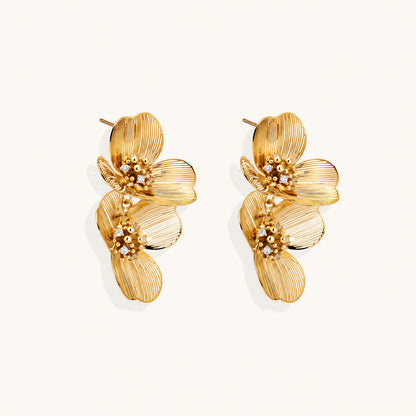 Pair of gold-plated double flower earrings with textured petals and crystal centers on cream background.