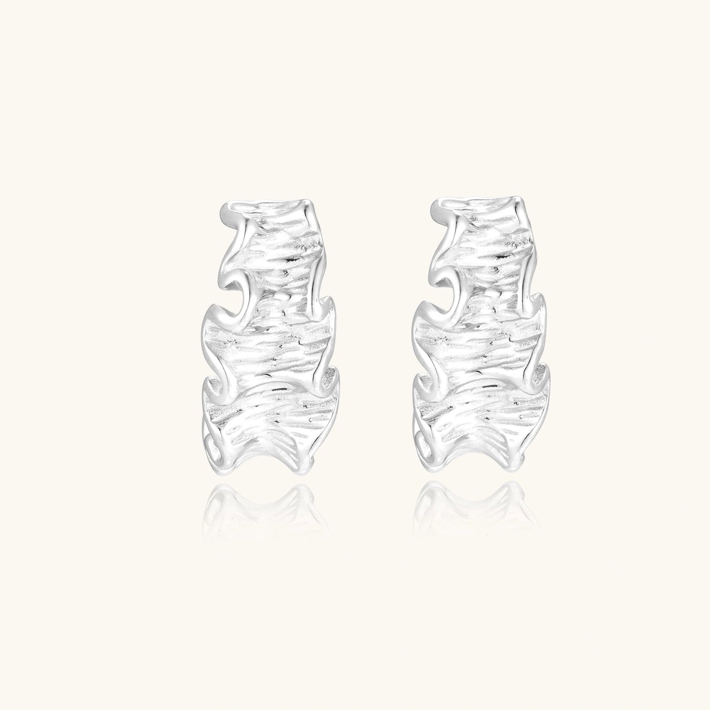 White gold plated sculptural hoop earrings with organic wavy edges and reflective metallic finish on cream background