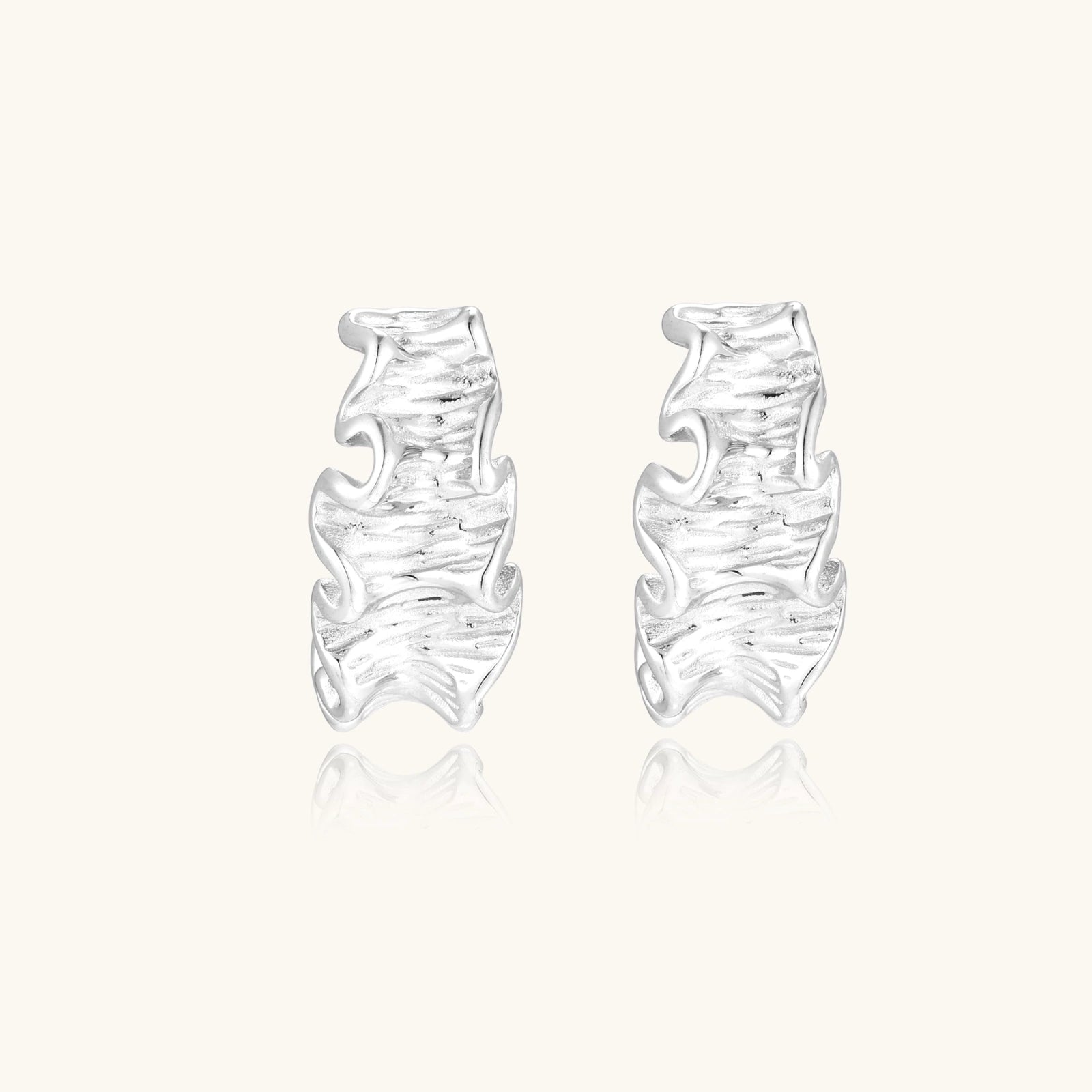 White gold plated sculptural hoop earrings with organic wavy edges and reflective metallic finish on cream background