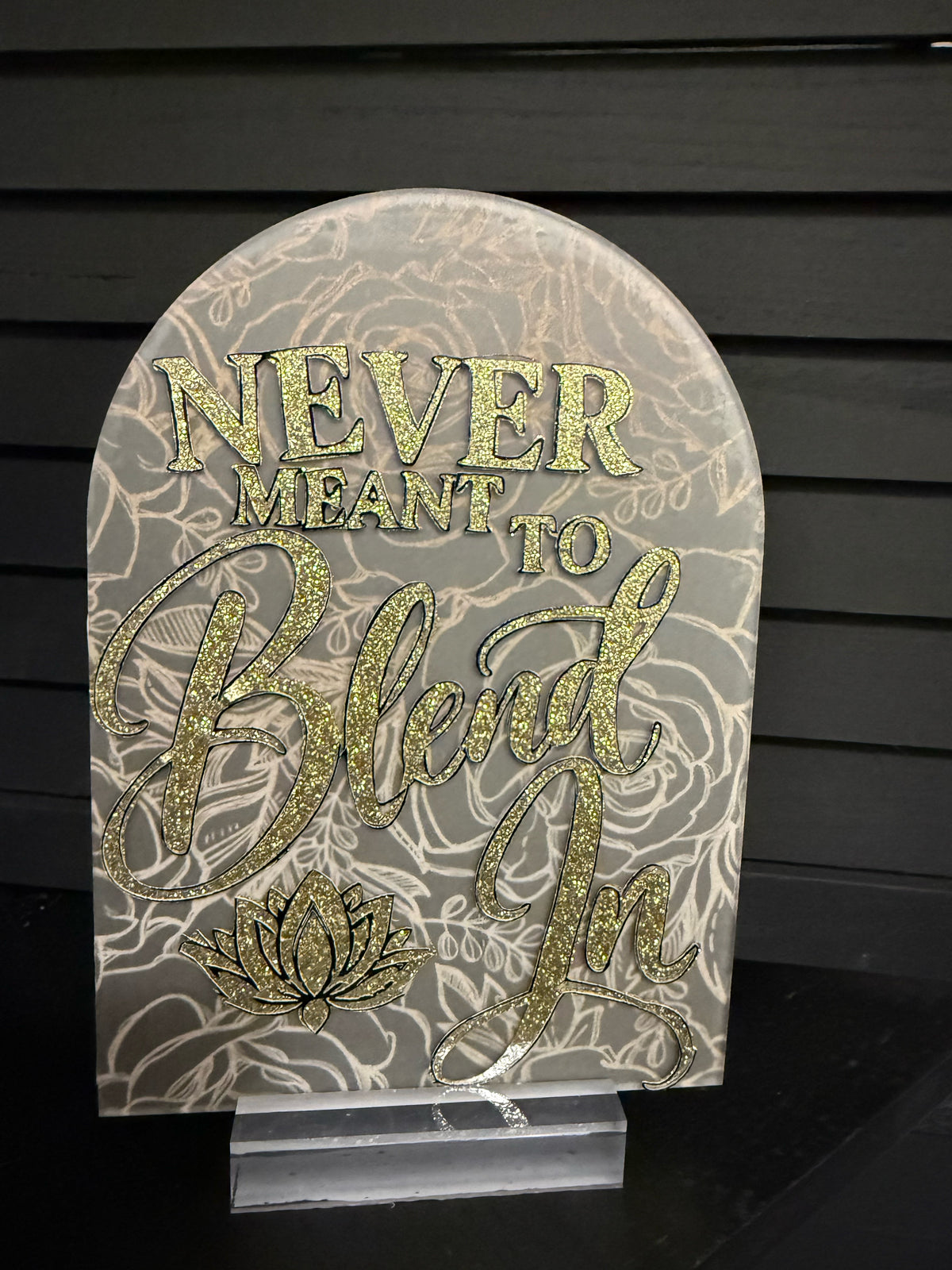 Never Meant to Blend In arched acrylic plaque: frosted clear with cream line-art roses, gold glitter lettering and gold glitter lotus, on a clear acrylic stand