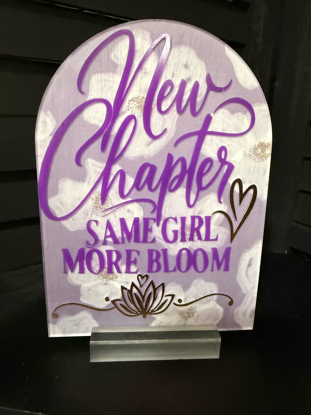 New Chapter Same Girl More Bloom arched acrylic plaque: lavender with white florals, purple script, gold foil heart and lotus, on a clear acrylic stand